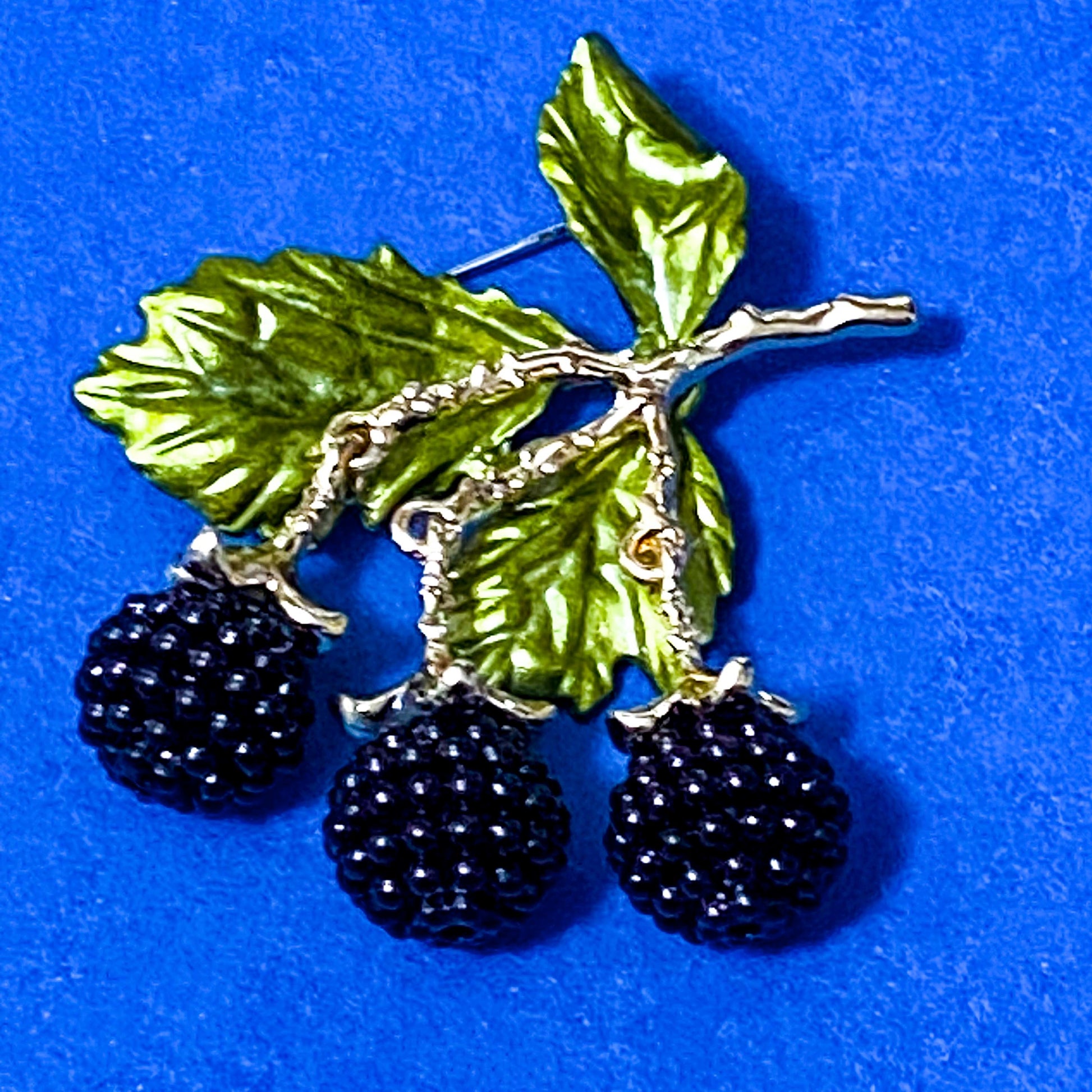articulated blackberry brooch with green leaves and gold tone metal on a dark blue background