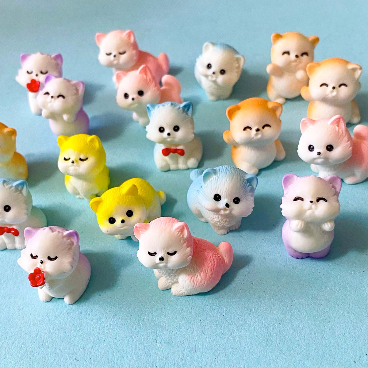 selection of miniature resin pastel kitten figurines in pink, lilac, blue, yellow and peach colours displayed on a pale blue background