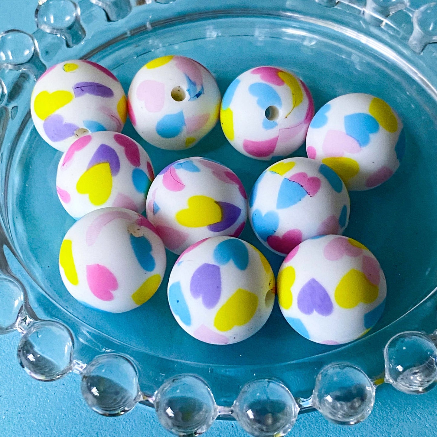 16mm round silicone white beads with a scattered hearts pattern in shades of blue, lilac, yellow and pink.