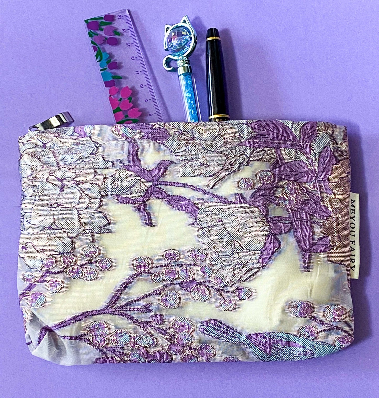 wisteria veil luxury woven tapestry cosmetic pouch with an ivory background and lavender and lilac botanical design, shimmering pale pink-lilac metallic threads, cream fabric lining and concealed zip.