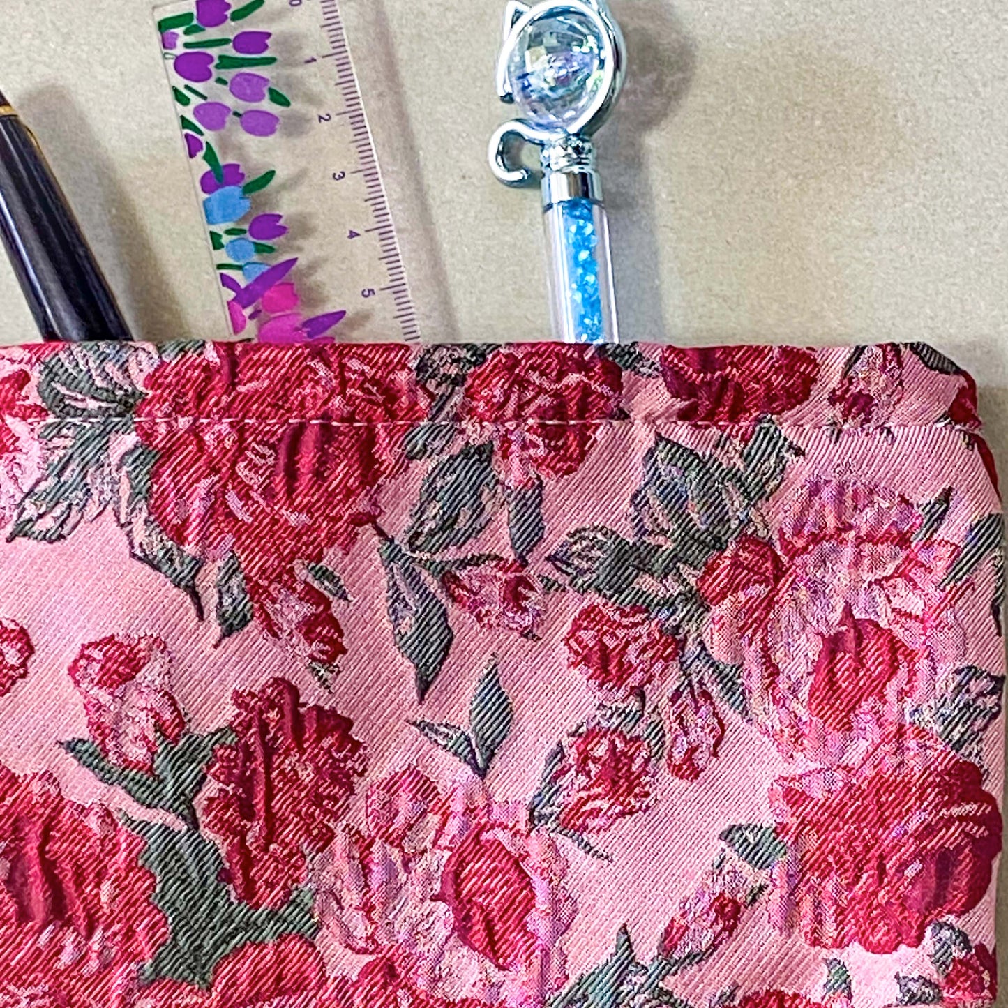 vintage rose arbour textured woven fabric tapestry make up pouch in smaller size with pink and red roses on pale pink background with soft green leaves. fully lined in cream fabric with concealed zip and gusset for space. uk letterbox gifts.