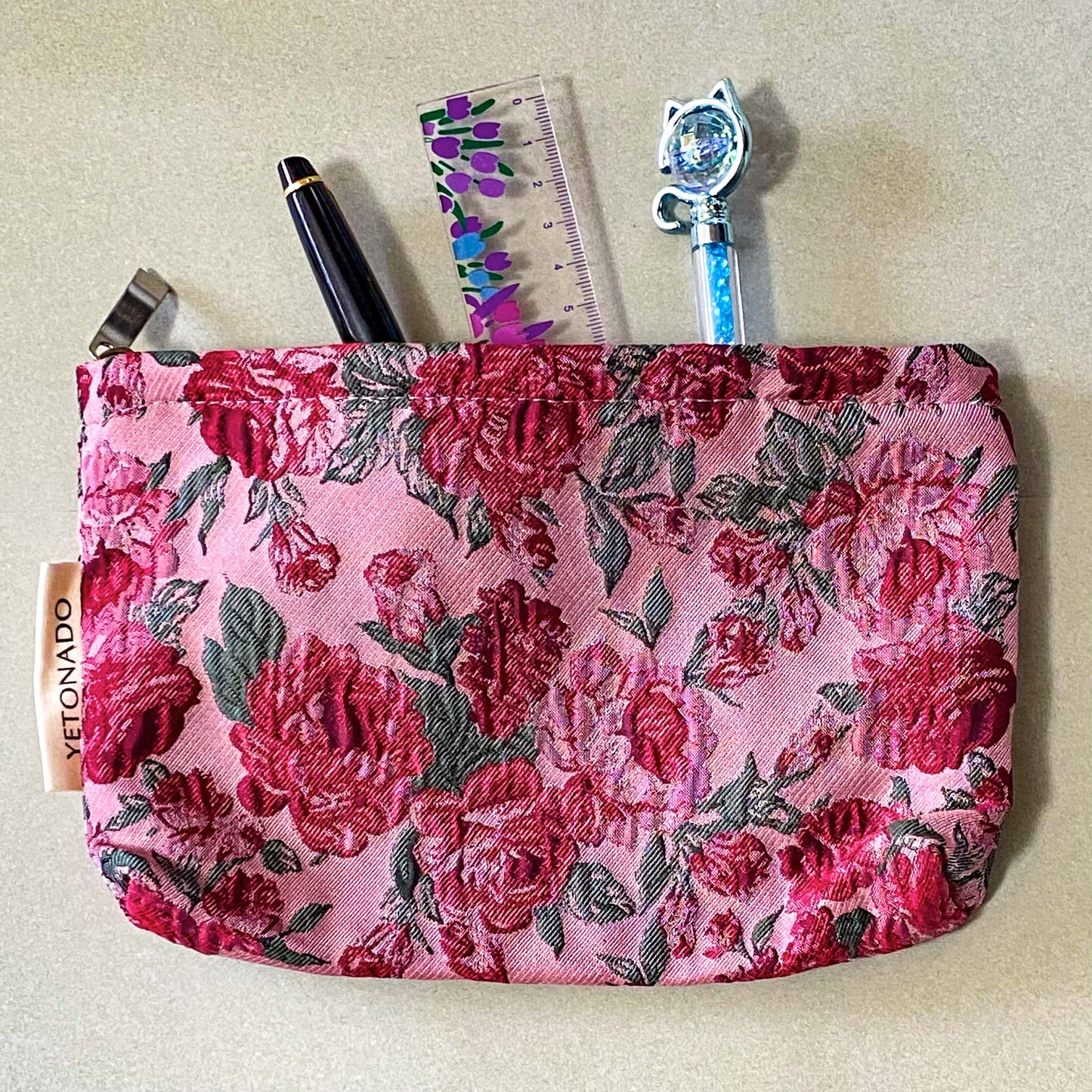 vintage rose arbour textured woven fabric tapestry make up pouch in smaller size with pink and red roses on pale pink background with soft green leaves. fully lined in cream fabric with concealed zip and gusset for space. uk letterbox gifts.