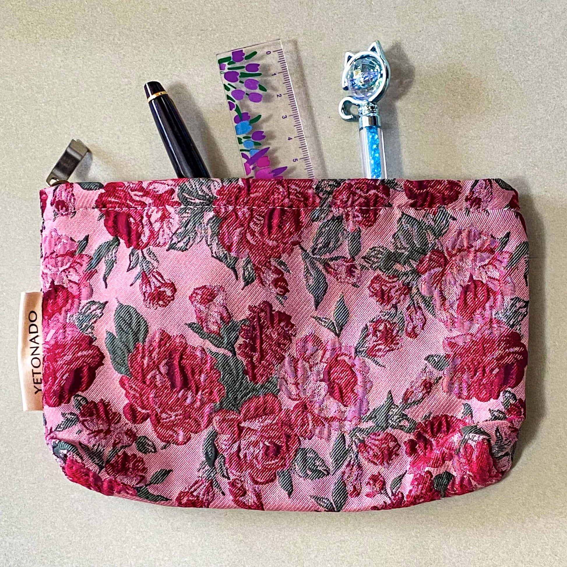 vintage rose arbour textured woven fabric tapestry make up pouch in smaller size with pink and red roses on pale pink background with soft green leaves. fully lined in cream fabric with concealed zip and gusset for space. uk letterbox gifts.