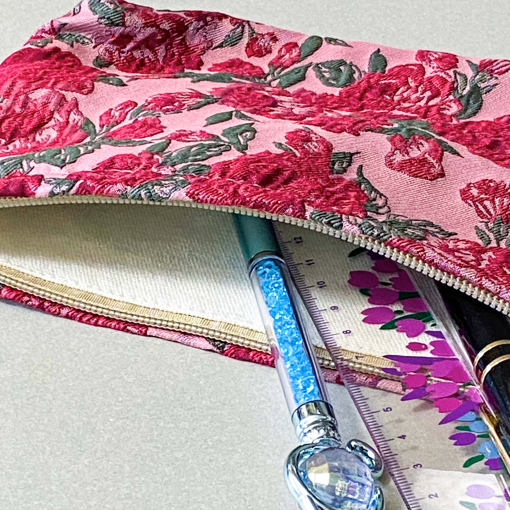 vintage rose arbour textured woven fabric tapestry make up pouch in smaller size with pink and red roses on pale pink background with soft green leaves. fully lined in cream fabric with concealed zip and gusset for space. uk letterbox gifts.