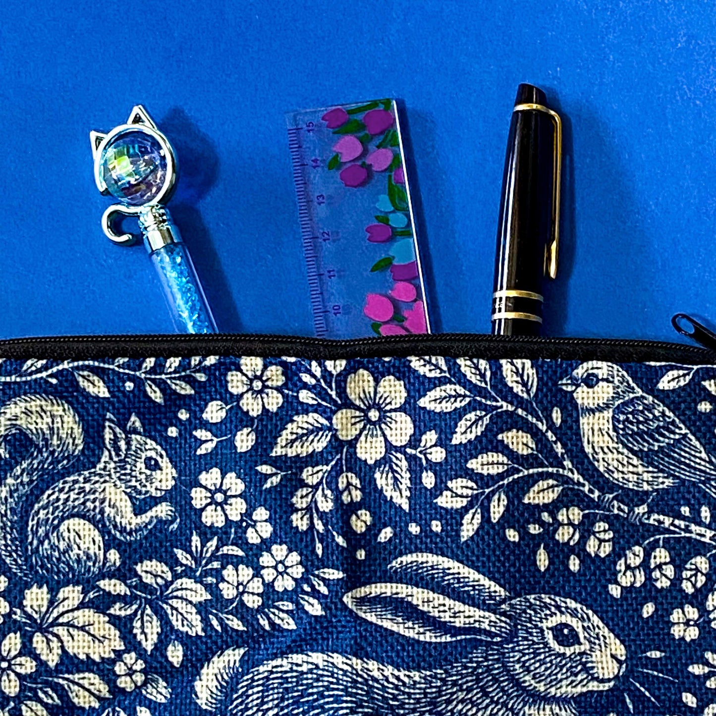 navy blue zip pouch made of canvas with a deep blue and cream design featuring a running hare, squirrel, bird and hedgehog among flowers and mushrooms in a forest scene. Uk letterbox gifts.