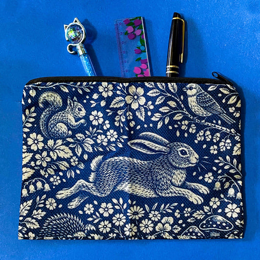 navy blue zip pouch made of canvas with a deep blue and cream design featuring a running hare, squirrel, bird and hedgehog among flowers and mushrooms in a forest scene. Uk letterbox gifts.