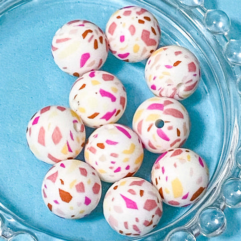 Colourful speckled pink and yellow abstract silicone beads on a blue glass plate