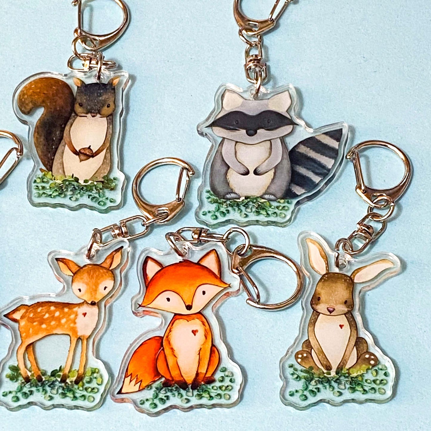Set of animal-themed keychains including a deer squirrel raccoon bunny and fox on a light blue background 