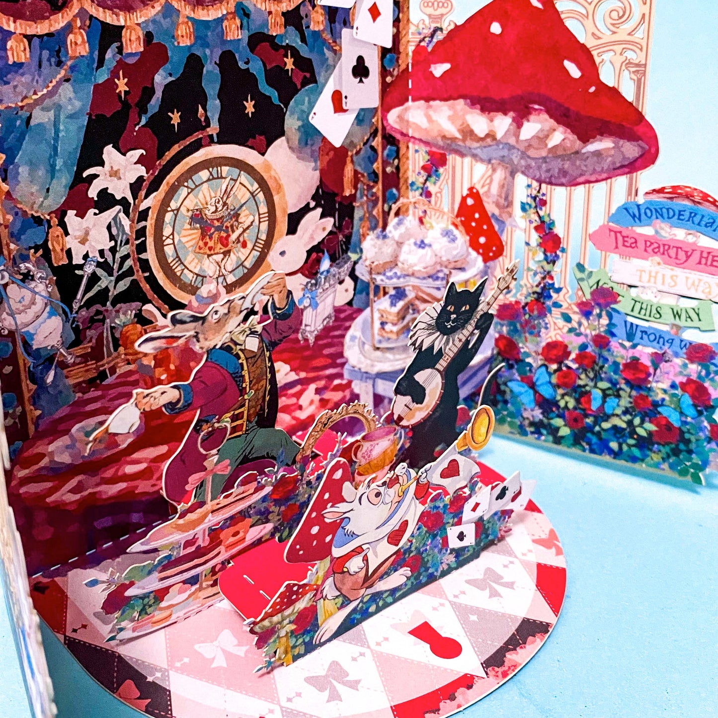 alice in wonderland themed pop up 3d greeting card with tea party scene, white rabbit, mushroom, playing cards and layered theatrical paper design.