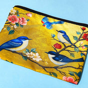yellow and blue zip fabric pouch with blue birds and floral branches used as a pencil case on a light blue background