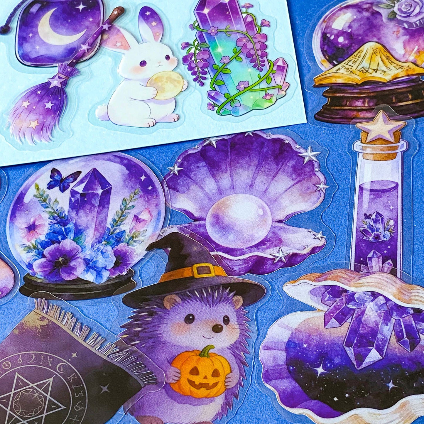 pack of 50 magical fantasy stickers featuring crystal balls, spell books, moonlit scrolls, enchanted mushrooms, ravens, potion bottles, celestial moons, magical animals and crystal gardens in lavender, violet and blue tones. UK stationery shop and letterbox gifts store.