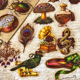 pack of 50 victorian inspired clear PET ephemera stickers featuring antique books, clocks, perfume bottles, roses, swans, butterflies, crowns, handwritten letters and curiosity cabinet treasures in rich dark burgundy, gold, green and midnight blue tones. Uk stationery shop.