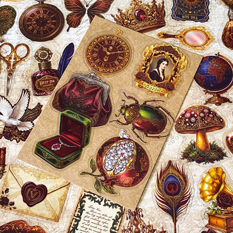 pack of 50 victorian inspired clear PET ephemera stickers featuring antique books, clocks, perfume bottles, roses, swans, butterflies, crowns, handwritten letters and curiosity cabinet treasures in rich dark burgundy, gold, green and midnight blue tones. Uk stationery shop.