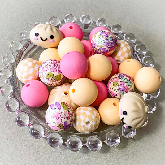 a coordinated bundle of 8 pastel silicone beads featuring one smiling jumbo dumpling bead, floral patterned beads and checkerboard beads, plain pink and cream beads. uk craft supplies.