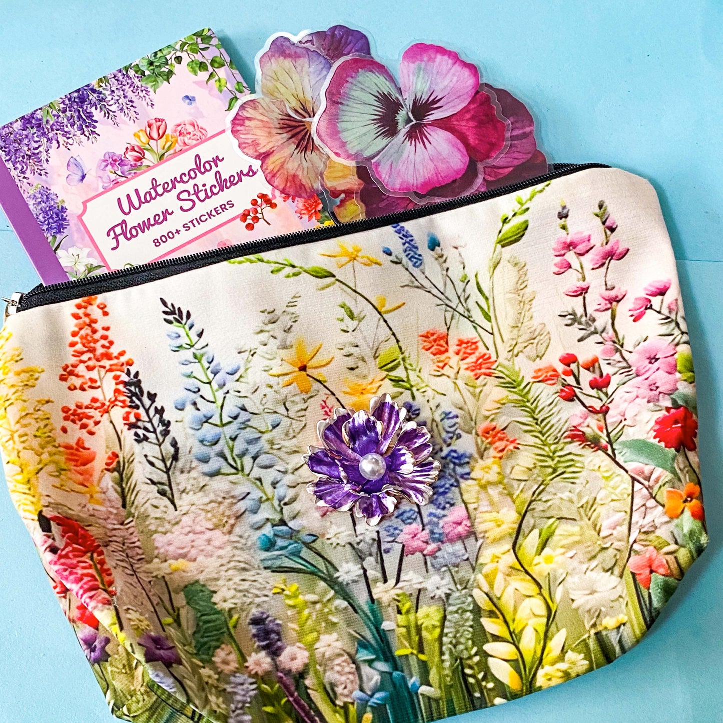 floral gift set with illustrated flower pouch, watercolour sticker book and purple enamel flower brooch on a blue background