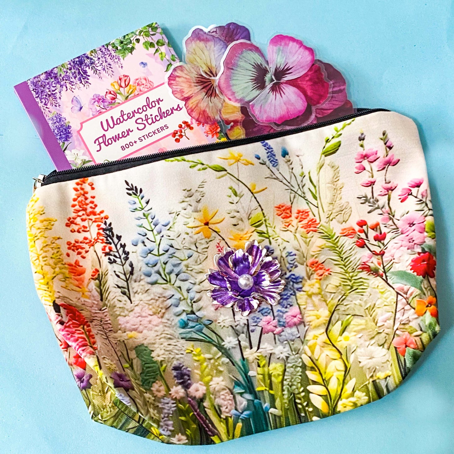 floral gift set with illustrated flower pouch, watercolour sticker book and purple enamel flower brooch on a blue background