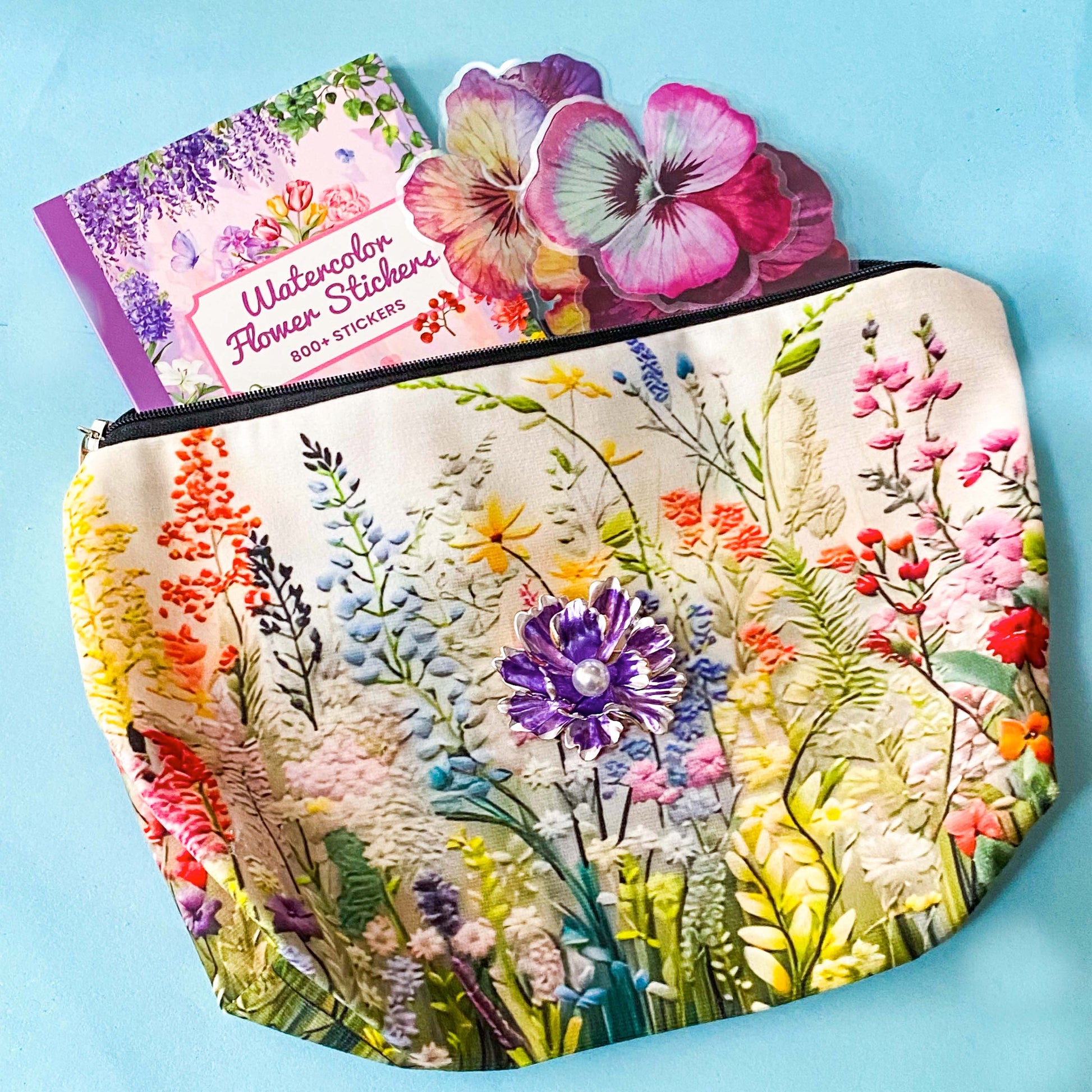 floral gift set with illustrated flower pouch, watercolour sticker book and purple enamel flower brooch on a blue background