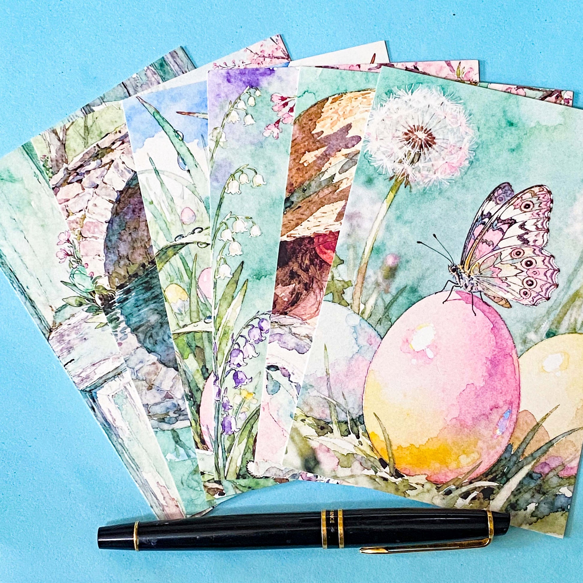 set of spring pastel postcards wrapped in a kraft belly band with wax seal sticker on a blue background including butterfly, easter eggs, girl with flowers and wreath 
