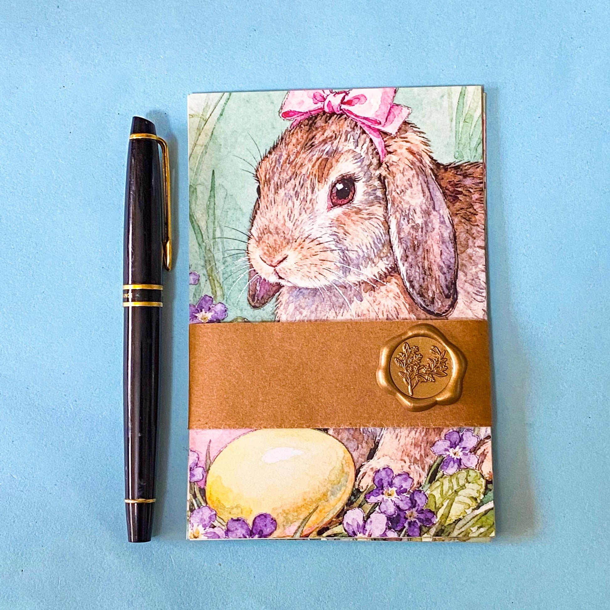 set of 6 spring animal postcards featuring bunny, blue bird, bee, squirrel and hedgehog illustrations with blossom flowers, wrapped in a kraft belly band with wax seal sticker on a soft blue background
