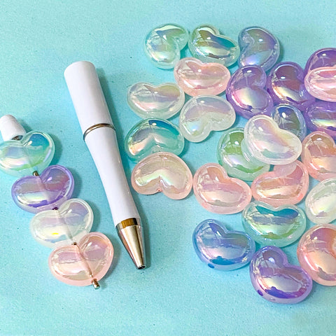 large iridescent 22mm by 16mm acrylic heart beads in pastel colours with a beaded pen base on a blue background