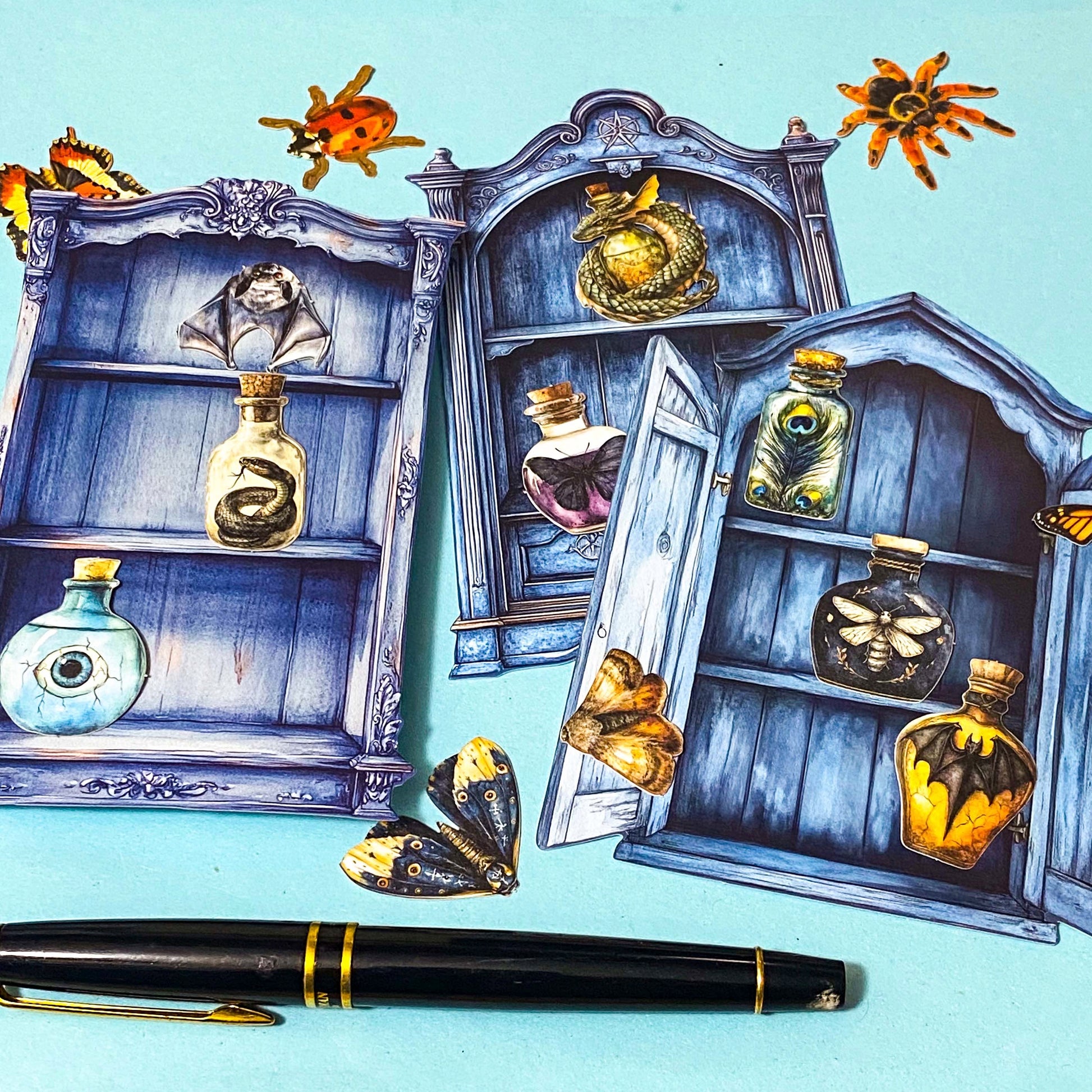 nature themed magic cabinet ephemera set with blue illustrated cabinet shelves and 22 paper cut put pieces including moths, insects and specimen bottles on a blue background with a pen