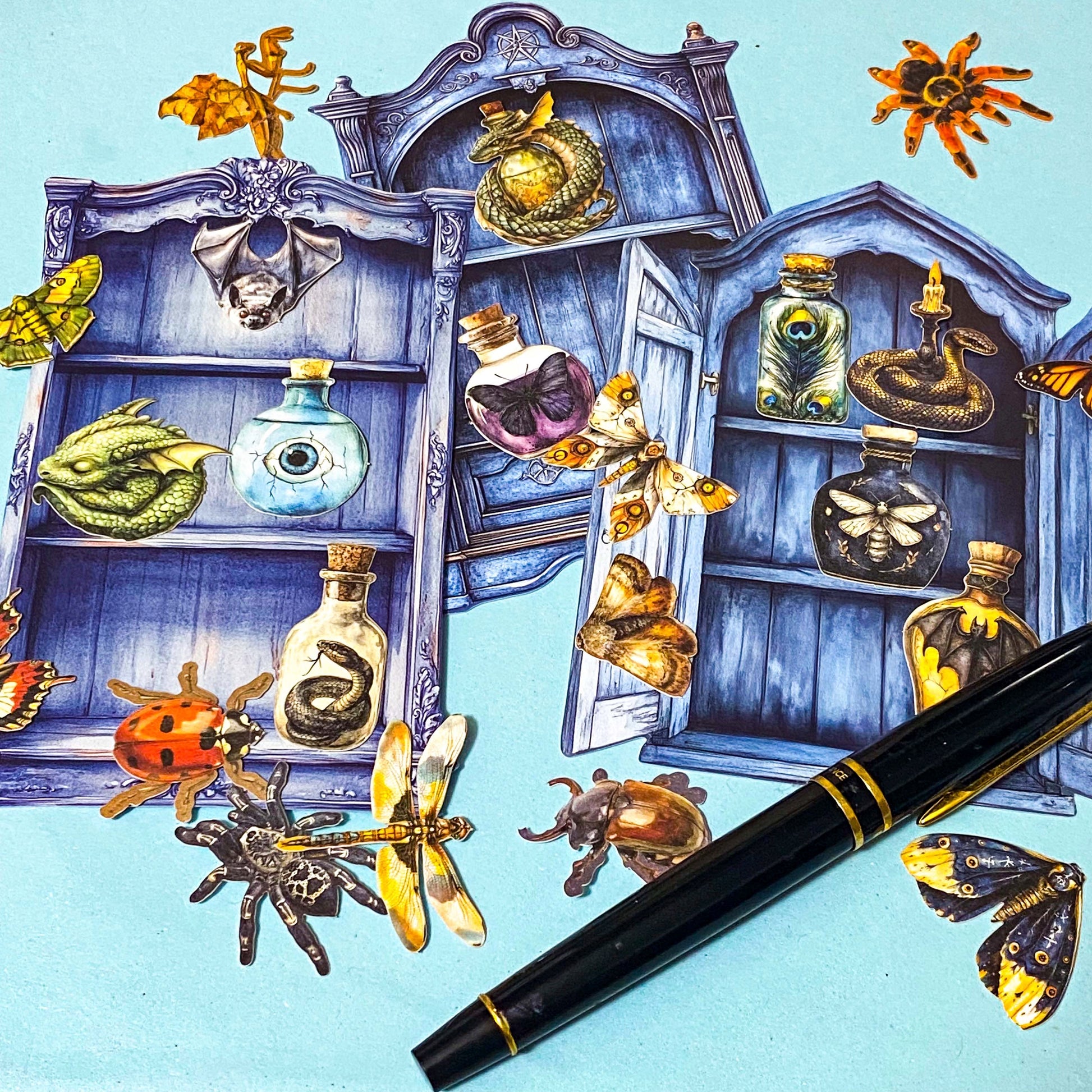 nature themed magic cabinet ephemera set with blue illustrated cabinet shelves and 22 paper cut put pieces including moths, insects and specimen bottles on a blue background with a pen