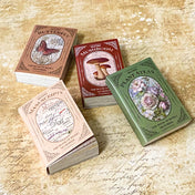 mini vintage scrapbooking paper and vellum books in botanical, butterfly, mushroom and manuscript designs displayed on a antique background