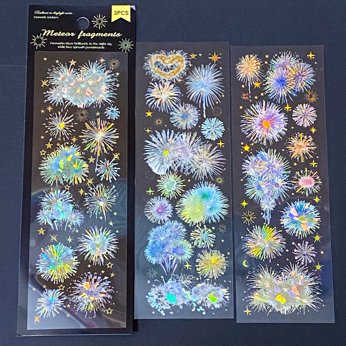 three transparent holographic firework sticker sheets with celestial stars, moons and iridescent rainbow foil effects