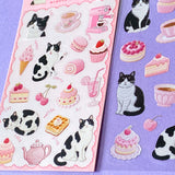 two assorted clear PET sticker sheets with black and white cats, pink cakes, pastries, tea cups and sweet cafe illustrations