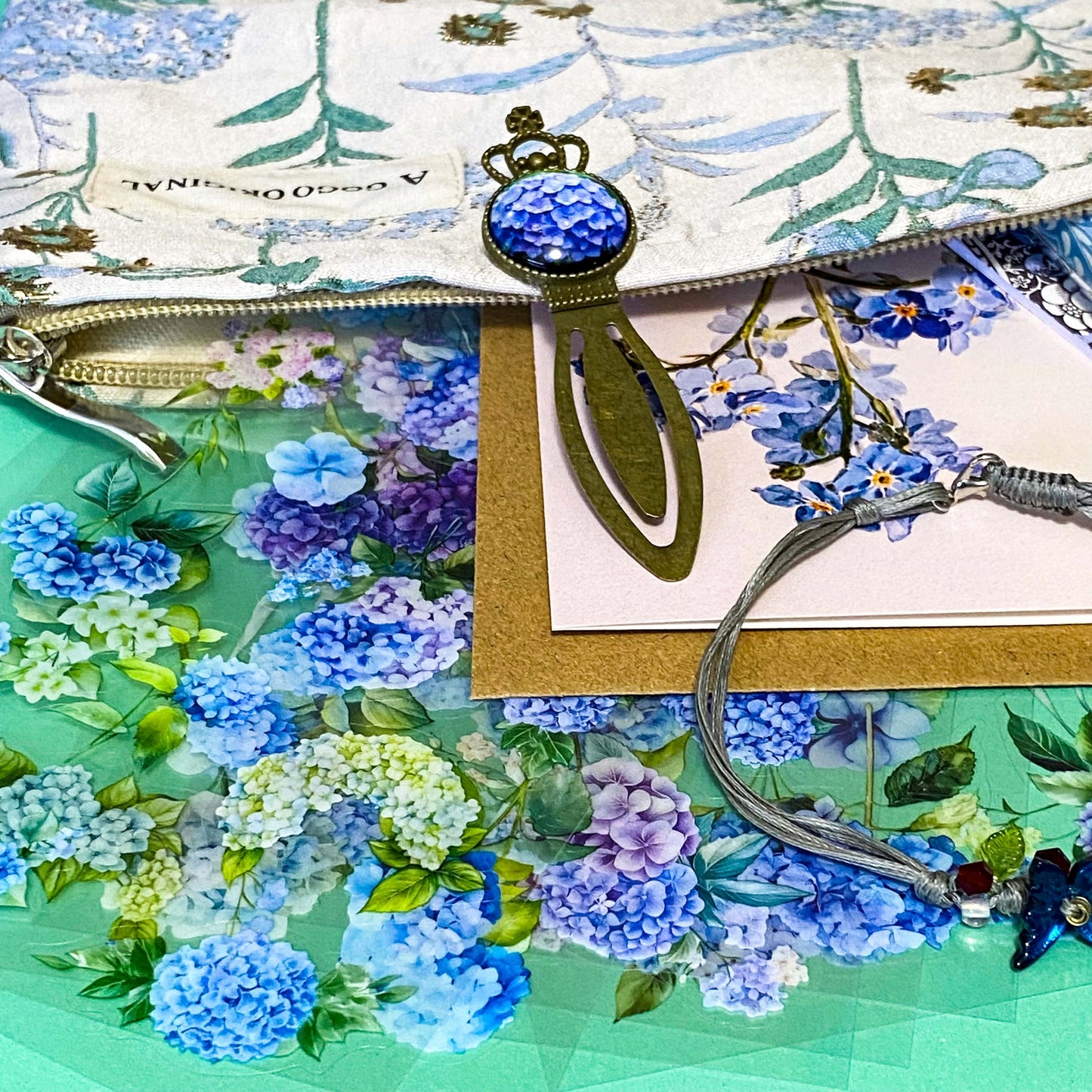 satin hydrangeas letterbox gift set with a lined satin-finish hydrangeas pouch, floral crystal bracelet, notebook, black ballpoint pen, metal bookmark,  2 hydrangea blank note cards and floral sticker sheets. 