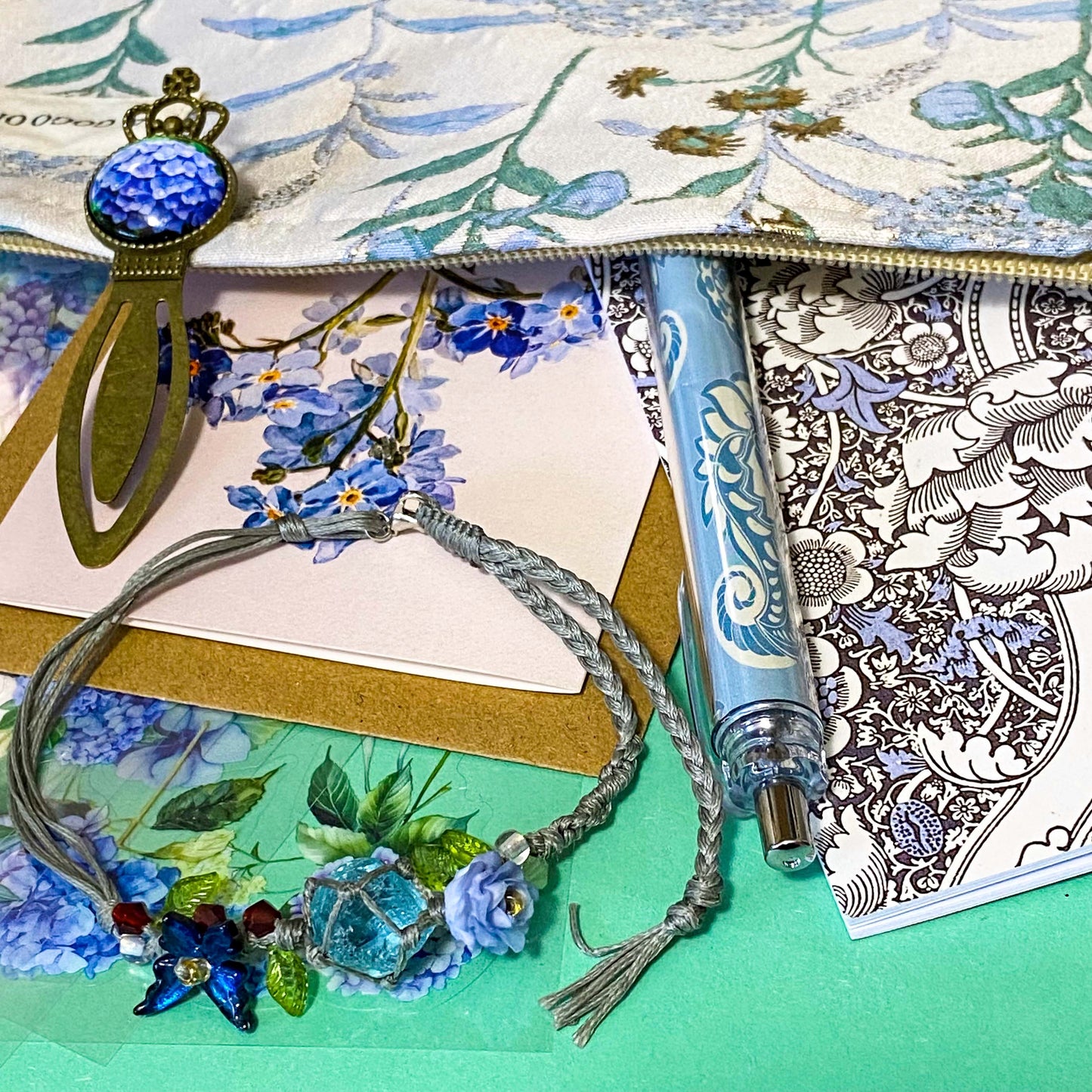 satin hydrangeas letterbox gift set with a lined satin-finish hydrangeas pouch, floral crystal bracelet, notebook, black ballpoint pen, metal bookmark,  2 hydrangea blank note cards and floral sticker sheets. 