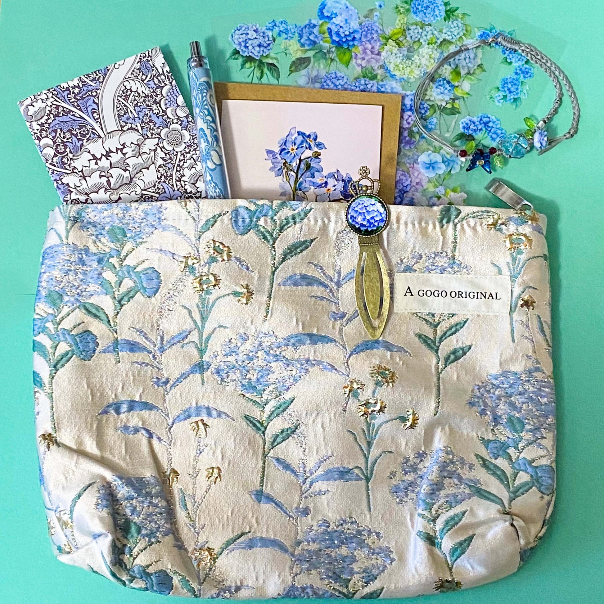 satin hydrangeas letterbox gift set with a lined satin-finish hydrangeas pouch, floral crystal bracelet, notebook, black ballpoint pen, metal bookmark,  2 hydrangea blank note cards and floral sticker sheets. 