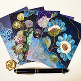 set of five jewel toned botanical postcards in deep blue and teal floral designs with gold-style detailing, styled with a black pen and wax seal on neutral background