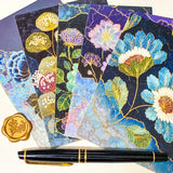 set of five jewel toned botanical postcards in deep blue and teal floral designs with gold-style detailing, styled with a black pen and wax seal on neutral background