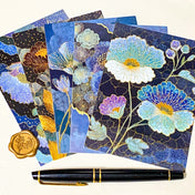 set of five jewel toned botanical postcards in deep blue and teal floral designs with gold-style detailing, styled with a black pen and wax seal on neutral background