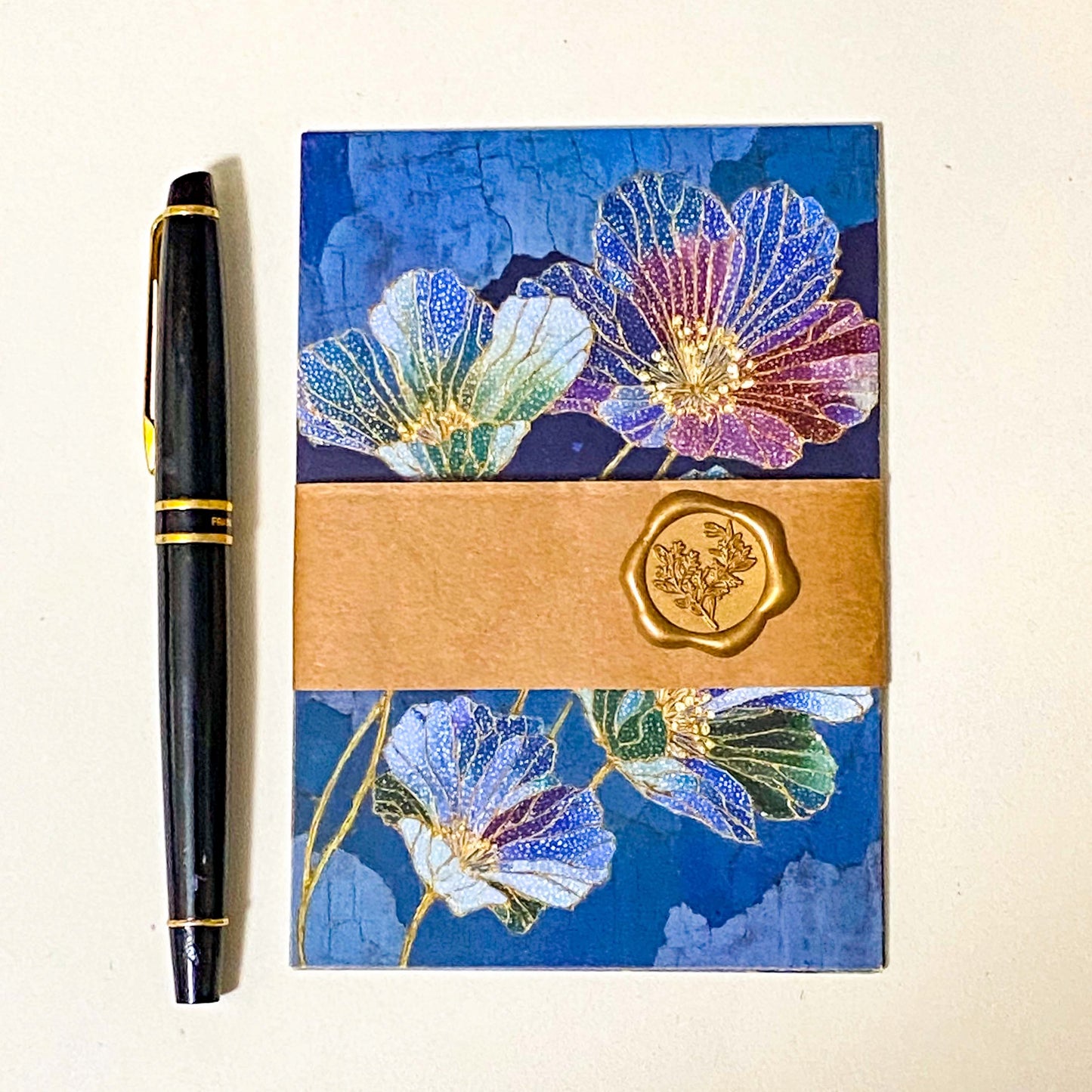 set of five jewel toned botanical postcards in deep blue and teal floral designs with gold-style detailing in a kraft belly band with wax seal sticker and pen