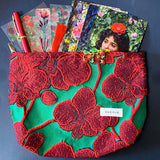 strawberries and red roses letterbox gift set featuring a lined emerald green and crimson floral pouch, rose sticker sheets, floral acrylic bookmark with tassel, red metallic pen, romantic postcards and enamel strawberry brooch. Uk letterbox gifts shop.
