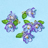 Purple flower-shaped acrylic charms with green leaves on a light blue background
