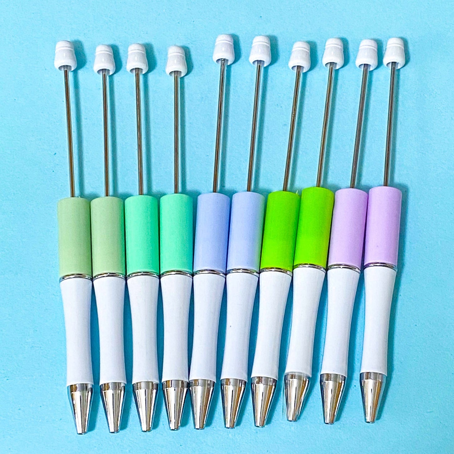 pastel beaded pen bases in sage, mint, periwinkle, lime and lavender on a blue background