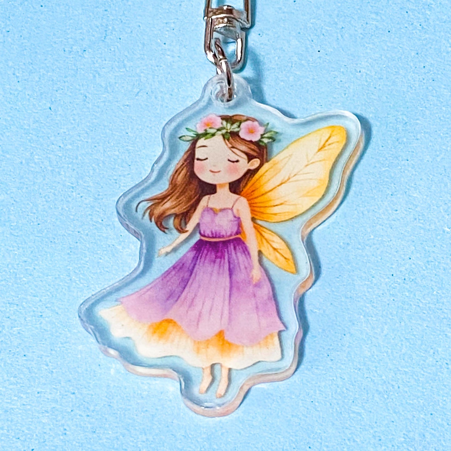 Fairy keychain with purple dress and yellow wings on a light blue background