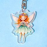 Fairy keychain with pink wings and a green dress on a light blue background