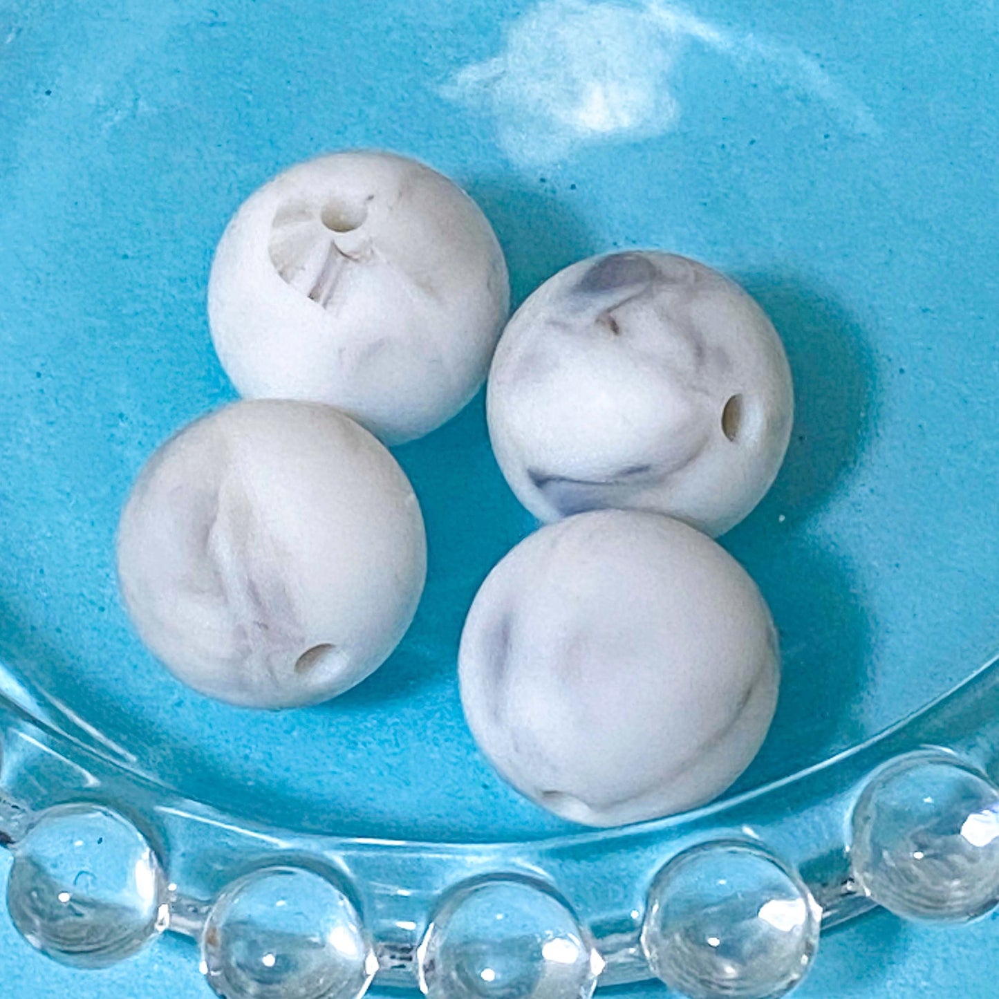White silicone marbled 16mm round beads on a blue background