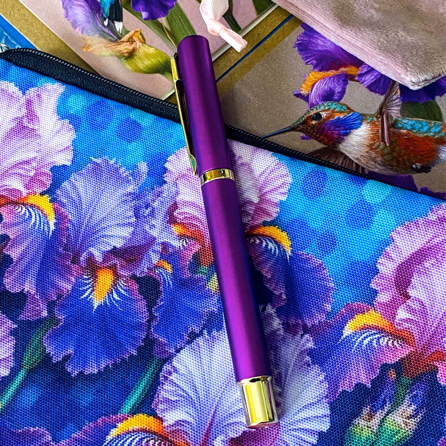 botanical iris letterbox gift set with waterproof floral pouch, purple metal pen, enamel iris brooch in pink velvet bag, clear floral stickers and hummingbird greetings cards. purple, deep jewel blue, lilac and magenta coloured flowers.