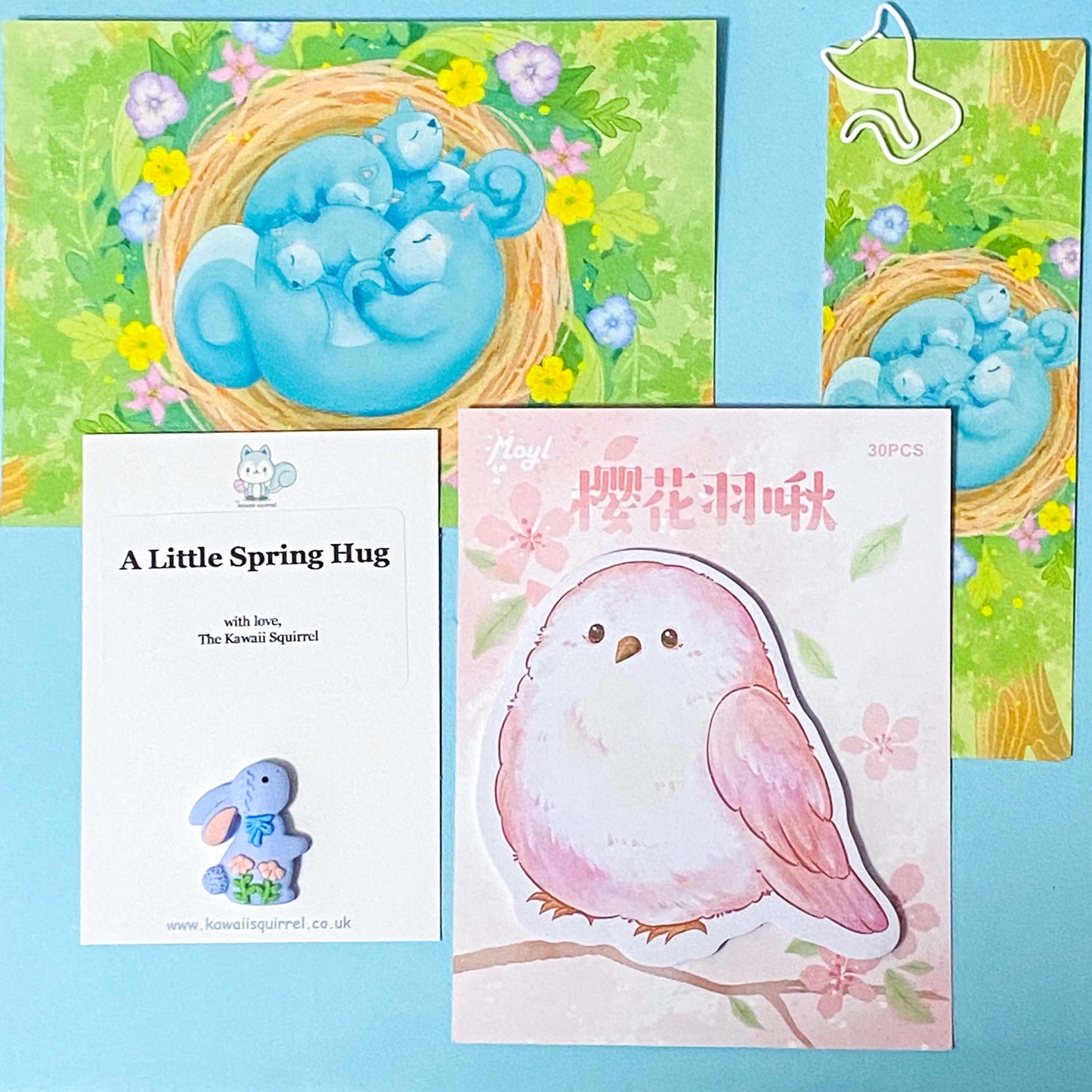 a pink spring bird memo with a postcard, a bookmark and a bunny pocket hug on a blue background