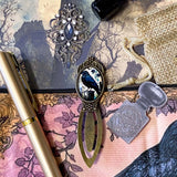 gothic raven themed letterbox gift set with ornate crow fabric pouch, gold metal pen, enamel raven pin brooch, vintage metal bookmark, dark paper stickers and scrapbook papers. Uk gift shop with mystical and witchy gifts.