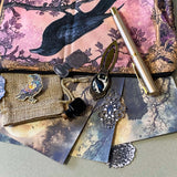 gothic raven themed letterbox gift set with ornate crow fabric pouch, gold metal pen, enamel raven pin brooch, vintage metal bookmark, dark paper stickers and scrapbook papers. Uk gift shop with mystical and witchy gifts.