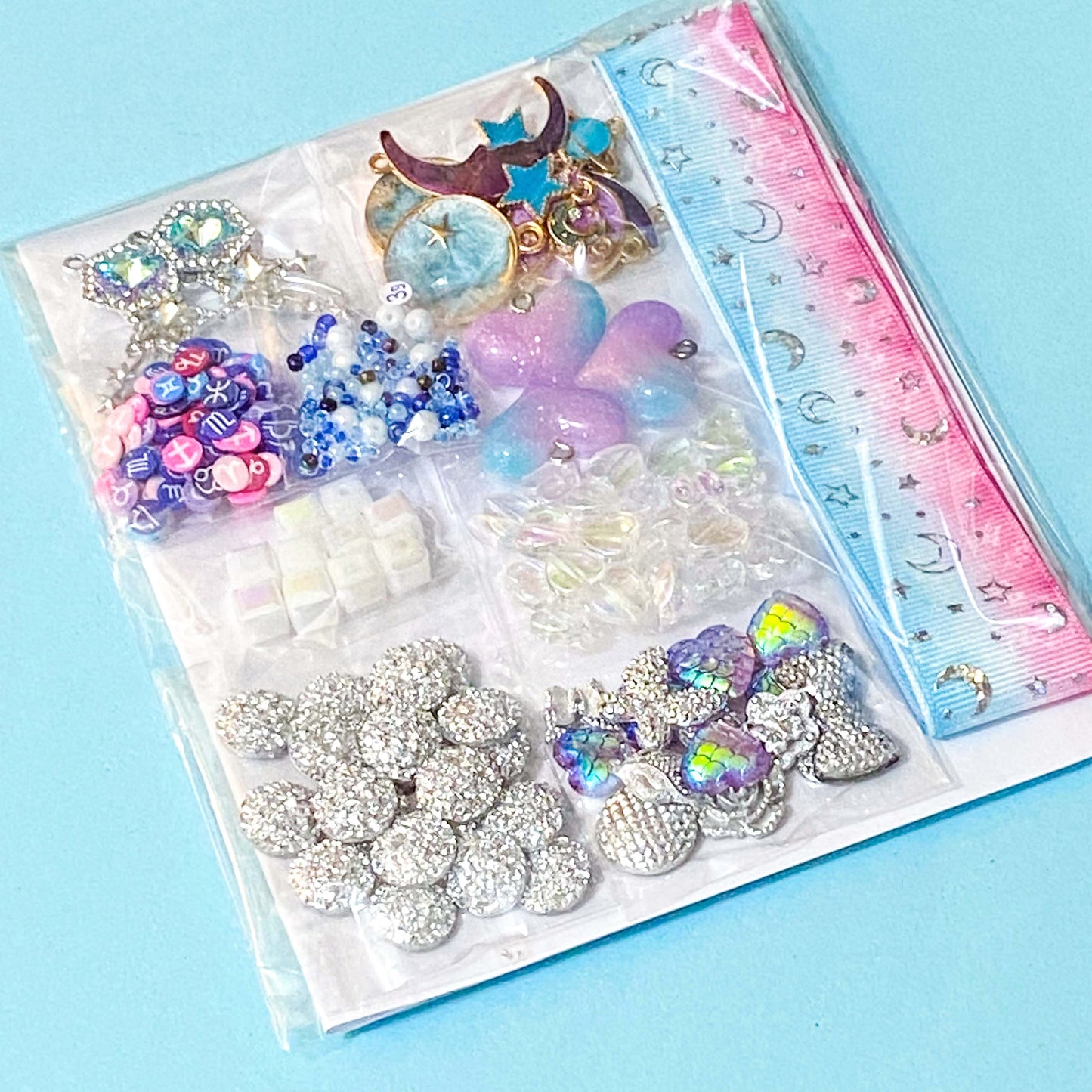 Assorted decorative charms and embellishments with a celestial space theme in a clear plastic bag on a blue background