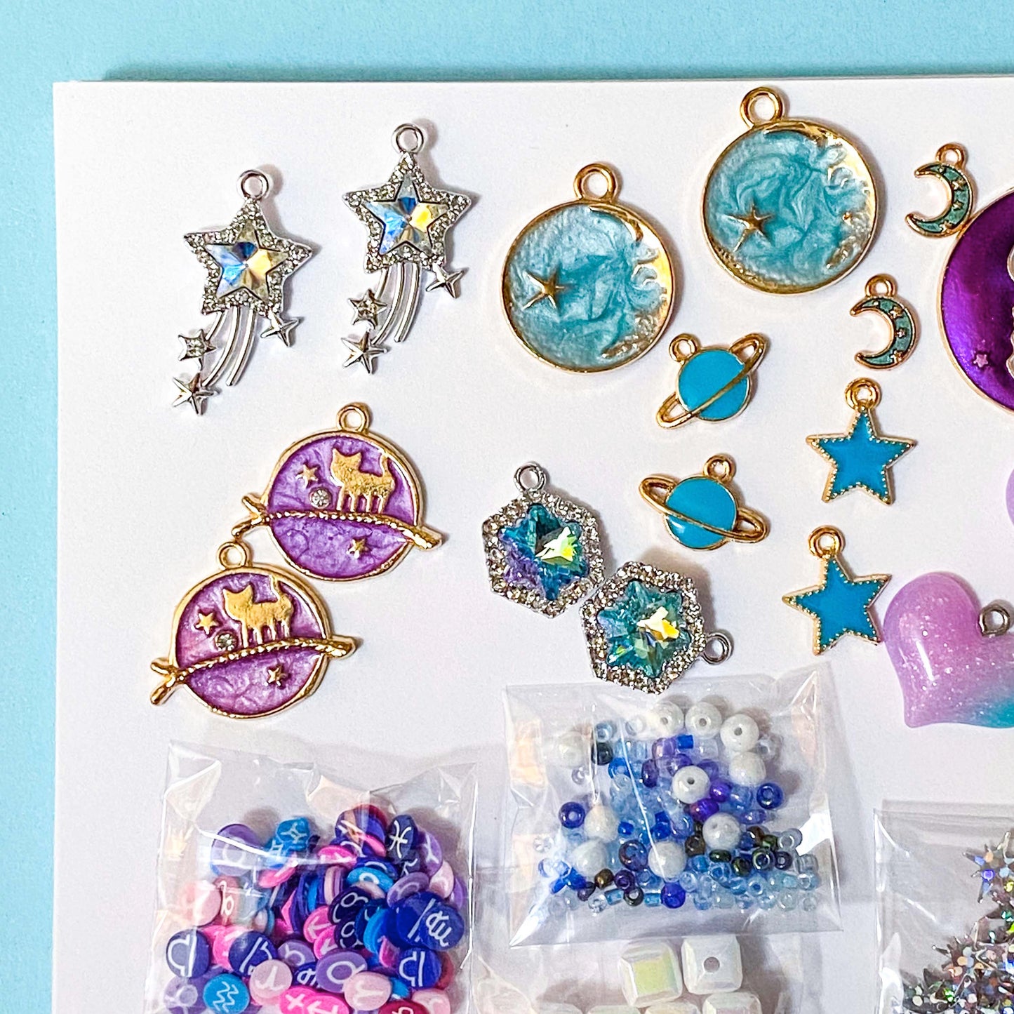 Assorted colorful jewelry charms and beads on a white card with a blue background. A craft bundle with a celestial theme