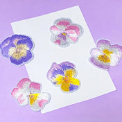 set of pastel embroidered pansy iron on fabric patches in pink, purple and yellow tones on soft background