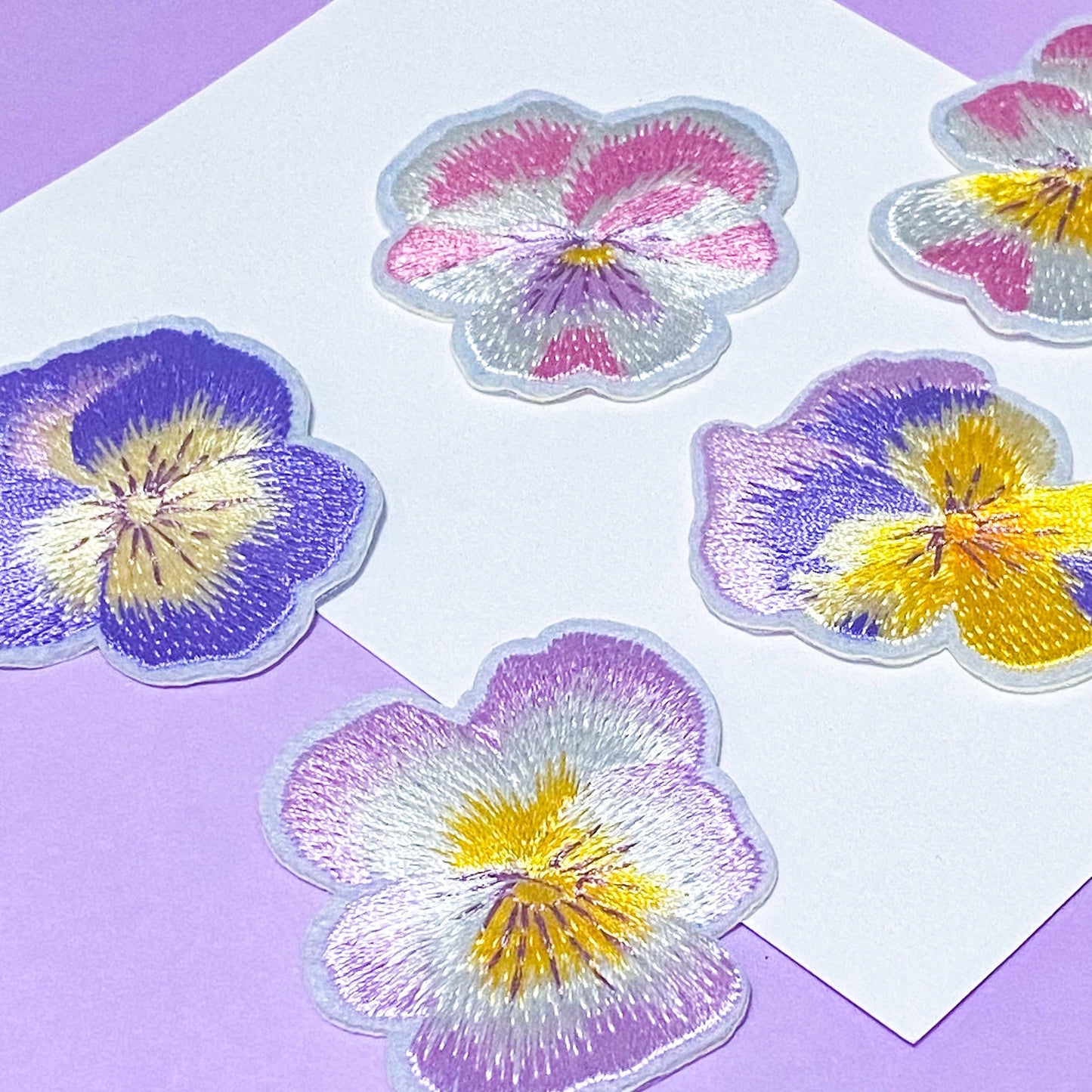 set of pastel embroidered pansy iron on fabric patches in pink, purple and yellow tones on soft background